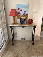 Front view of side table with metal base and beige stone top, lamp and decorative items on top.