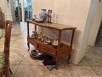 Wood side table with stone top against wall, showing front with drawers and lower shelf. Decorative items on top and shelf not included.