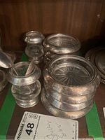 Eight sterling silver bordered glass coasters stacked with two glass and silver candle holders nearby.