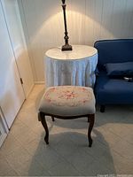 Round table with light colored cloth draped over it, glass top under cloth, and wooden base, positioned beside blue sofa and door.