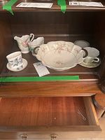 Porcelain serving bowl, creamer, sugar holder, and five teacups with matching saucers, all with floral patterns displayed inside a wooden cabinet.