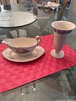 Photo of both vintage Wedgwood items on pink placemat: gravy pitcher with plate and tall decorative vase