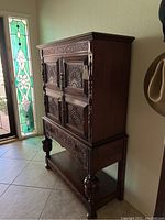 Side angle showing full height, ornate carved panels on doors, drawer, and legs, plus solid wood construction.