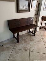 Wood bench placed against a wall, showing spiral carved legs and ornate backrest.
