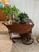 Side view of the wooden tea cart, showing the turned legs, large wooden wheels, and contents on top and bottom shelf.