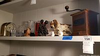 Shelf showing assorted art glass, figurines including ceramic dog, black dancing couple, wooden figurines, and vintage wooden coffee grinder
