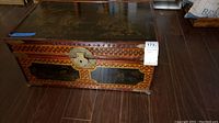Front and sides of wooden chest showing brass lock and woven pattern framing lacquer panels