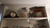 Full shelf view showing 5 clocks on a white shelf including Seth Thomas mantel clock, metal frame clocks, gold-tone clock, and wooden case clock.