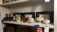 Shelf with framed wall art, assorted figurines, bowls, and glassware including small ceramic pieces and decorative lidded jars.