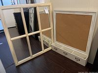 Overall angled view showing both framed mirror and message board with shelf side by side on floor.