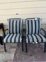 Front view of two black metal patio chairs with black, white, and gray vertical striped cushions.