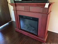 Front view of the electric fireplace showing the faux log interior and red wooden mantel with detailed molding.