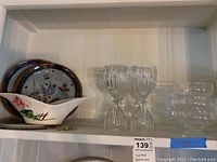Full shelf view showing 6 stemmed glasses, 6 dessert cups, decorative ceramic dish, and 2 oval ceramic trays.