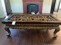 Front view of the carved wood coffee table showcasing entire tabletop relief panel and legs