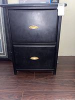 Front view of black wood filing cabinet showing two drawers and brass handles.