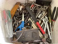 Wide view of box filled with assorted wrenches, scissors, screwdrivers, pliers, and metal hardware