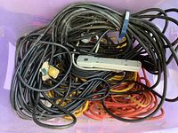 Large assortment of coiled extension cords in black, orange, and yellow, along with a white 4-outlet power strip inside a purple container.