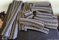 Photo shows multiple metal O gauge train tracks spread out on a flat surface. Tracks include straight and curved sections in various lengths.