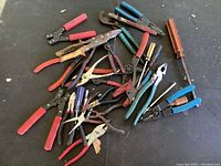 Top view photo showing a large mixed assortment of hand tools including crimpers, pliers, wire cutters, and screwdriver arranged on a gray floor surface.