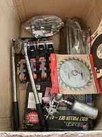 Box showing visible ratcheting tie downs, ratchet handle, pneumatic air die grinder, and circular saw blade packaging