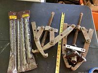 Photo shows two large industrial pullers with rusted metal and adjustable arms along with a tape measure for size reference.