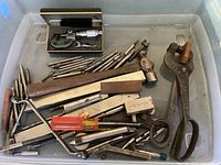 Top view of assorted mechanist tools in plastic container showing micrometer, steel rulers, hammer, pliers, files, screwdrivers, and other hand tools