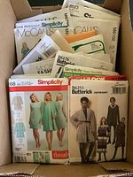 Box containing a large collection of paper sewing patterns in envelopes from various brands including Simplicity, McCall's, Butterick, and Vogue