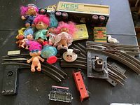 Full lot overview showing Troll dolls, Hess truck, Lionel train tracks and accessories, and miscellaneous items.