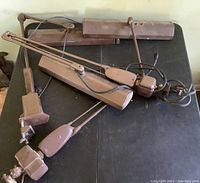 Three Mid-Century Modern industrial style desk lamps with brown metal adjustable arms and clamps, electrical cords included, placed on a black surface.