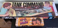 Photo showing two vintage game boxes: a large Tank Command game box and a smaller Mork & Mindy game box placed on a surface.