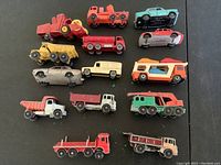 15 vintage Matchbox toy vehicles including fire trucks, dump trucks, cars, and campers arranged on a black surface along with several vintage Matchbox collectible cards.