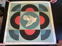 Full view of square print with geometric and bird design held by two hands, showing overall artwork and colors