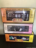 Three boxed Rail King freight cars for O and O-27 scale, showing front of the packaging with product information and window displays.
