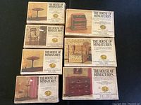 Seven sealed boxes of The House of Miniatures dollhouse furniture showing different pieces like chair, desk, bed, tables, dresser, and curtains.