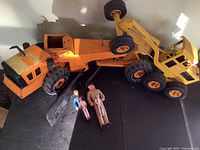Photo showing Tonka Mighty Grader toy with three vintage plastic action figures on black surface.