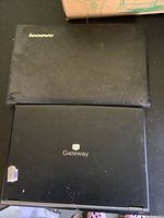 Photo showing two laptops stacked, Lenovo on top and Gateway below, both black and used condition.