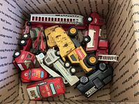 Box of assorted vintage toy trucks including fire chief theme, construction trucks, and a black Tootsie branded vehicle showing wear and paint chips