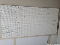 Full white pegboard panel with metal peg hooks attached, mounted on a wall.