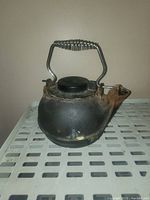 Front view of cast iron wood stove kettle showing rust, coil spring handle, spout, and removable lid