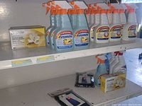 Multiple bottles of Dynamite spray bottles in white and blue, Compliments scented soap bars, and small packaged items on white shelves.