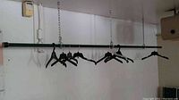 Clothes rack metal pole hanging from ceiling by chains with black hangers on the pole