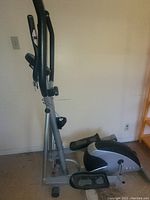 Side view of elliptical stepper showing pedal and handle setup with the front flywheel housing.