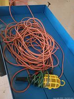 Coiled orange extension cord with yellow hanging work light placed inside a blue container.