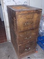 Front view of metal file cabinet showing three drawers with metal handles and label holders, heavy wear and patina visible.