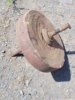 Photo of one antique stone wheel showing round shape, metal axle with handle, and surface chipping