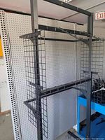 Front and side angled view of large metal retail display rack showing grid mesh panels and horizontal hanger bars