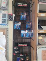 Full view of Panasonic battery display rack with multiple blue blister packs of AA and AAA alkaline batteries arranged on hooks.