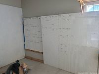 Three white peg boards leaning against a wall; two large and one small, with multiple metal peg hooks attached. Boards are approx. 20 feet in combined length.