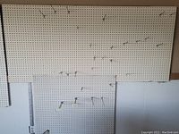 Two beige pegboard panels of different sizes mounted on wall with multiple metal hooks inserted into holes in the panels.