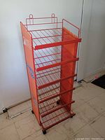 Front view of red metal wire shelving unit with angled shelves and wheels